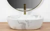 A close-up of a marble-patterned sink with a gold faucet, set against a white wall and a round mirror. Náhled obrázku produktu