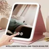 A hand is touching a makeup mirror with lights, which is folded open and standing on a desk. Produktbild-Vorschau