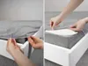 A split image showing hands putting a grey fitted sheet onto a mattress on a white bed frame. Anteprima dell’immagine prodotto