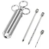 A stainless steel meat injector and three needles are displayed against a white background. Voir les images du produit