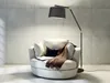 A modern floor lamp arches over a comfortable armchair in a minimalist living room setting. Náhled obrázku produktu