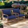 Two dark blue outdoor rocking chairs with wooden frames are placed on a patio with potted plants and string lights overhead. Produktbild-Vorschau