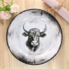 A plate with a bull's head design is placed on a wooden surface, with some decorative flowers and a rolled napkin nearby. Voir les images du produit