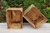 Two wooden crates are placed on a light-colored wooden surface with a green hedge in the background. Produktbild-Vorschau