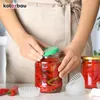A person is shown closing a jar of pickled red peppers with a green lid, with other jars and some small white paper cups on a table. Anteprima dell’immagine prodotto