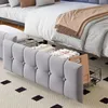 A close-up view of a bed with a gray upholstered headboard and storage drawers underneath. The bed is made with white and patterned bedding, and a beige throw blanket is draped over it. Storage baskets are visible under the bed. Anteprima dell’immagine prodotto