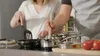Two people cooking together in a kitchen, with pots and pans on a stovetop. Produktbild-Vorschau