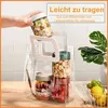A hand is placing a glass jar filled with food into a clear tote bag containing other jars of food. The scene is set on a wooden table with a plant and fruit in the background. Produktbild-Vorschau