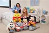 Two young women are sitting on a bed surrounded by various Disney Snackles plush toys. Anteprima dell’immagine prodotto