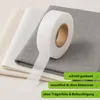 A roll of white hemming tape is shown on top of folded fabric swatches in different neutral colors. Produktbild-Vorschau
