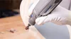 A gloved hand is using a Dremel tool to sand a wooden object. Produktbild-Vorschau