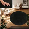 A round black rug is placed on a wooden floor in a living room setting, with furniture and plants around it. Produktbild-Vorschau