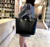 A woman is holding a black quilted leather tote bag in what appears to be a store or public space with bookshelves in the background. Náhľad obrázku produktu