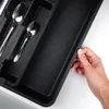A hand is shown placing a black cutlery organizer into a drawer. Produktbild-Vorschau