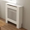 A white radiator cover with vertical slats is shown in a room with light gray walls and a wooden floor. Anteprima dell’immagine prodotto