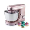 A rose gold stand mixer with a stainless steel bowl and a clear lid, shown with four decorative cupcakes in the foreground. Podgląd zdjęcia produktu