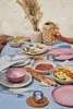 A table set for a meal outdoors, possibly on a beach or picnic setting, with food, drinks, and tableware. Náhled obrázku produktu