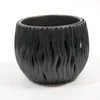 A black planter with a wavy, cut-out design sits on a white surface. Náhľad obrázku produktu