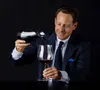 A man in a suit is pouring red wine from a decanter into a wine glass. Podgląd zdjęcia produktu