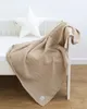 A beige muslin blanket draped over a white crib with a white star pillow in the background. Produktbild-Vorschau