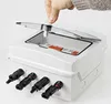 A hand is shown closing the lid of a white solar junction box. The box has four black MC4 solar connectors on the front. Podgląd zdjęcia produktu