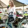 A woman is smelling a flower next to a bicycle at an outdoor market. Produktbild-Vorschau