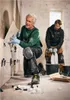Two men are tiling a wall in a room. One man is kneeling and placing a tile, while the other is standing and mixing grout. Produktbild-Vorschau