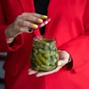 A person in a red jacket is holding a jar of pickles. Produktbild-Vorschau
