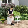 A woman is reading a book while sitting on a white ceramic stool in a garden. Anteprima dell’immagine prodotto