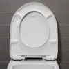 A close-up, top-down view of an open white toilet seat with a gray tiled wall in the background. Produktbild-Vorschau