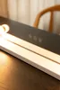 A close-up of a vanity mirror with integrated lighting and touch controls, resting on a wooden surface. Náhled obrázku produktu