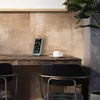 A weather station sits on a wooden desk next to a coffee cup, with chairs and a plant in the background. Produktbild-Vorschau