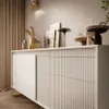 A close-up shot of a modern beige sideboard with decorative items on top, set against a textured wall and curtains. Produktbild-Vorschau