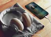 Headphones and a smartphone are placed on a wooden surface, with the smartphone connected to the headphones via a cable. Produktbild-Vorschau