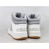 The back view of two white Adidas Hoops 3.0 Mid sneakers with gray accents and brown soles, placed on a light gray and white speckled surface. Produktbild-Vorschau
