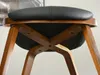 Close-up view of the underside of a wooden stool with a black seat. Voir les images du produit
