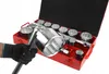 A hand wearing a black glove holds a large socket wrench, with a red toolbox filled with sockets in the background. Produktbild-Vorschau