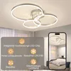 A modern LED ceiling lamp with multiple rings is shown installed on a ceiling, with a smartphone displaying a similar lamp in a bedroom setting. Podgląd zdjęcia produktu