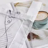 A close-up of a sheer curtain with embroidered details, placed over an open book, with a cup of coffee and a knitted blanket in the background. Produktbild-Vorschau