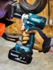 A person wearing work gloves is holding a Makita impact wrench, using it on a piece of machinery. Produktbild-Vorschau