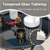 A close-up view of a black glass tabletop with decorative items, including a bottle, pinecone, berries, and a white vase. Produktbild-Vorschau