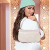 A young woman wearing a mint green beanie and a white t-shirt poses with a fluffy cream-colored mini pouch bag. Produktbild-Vorschau