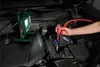 A person is using jumper cables to jump-start a car battery, with a work light illuminating the engine bay. Produktbild-Vorschau