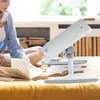 A young woman is studying on a bed with books and a laptop stand. Produktbild-Vorschau