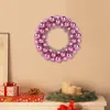 A pink and silver Christmas wreath hangs on a wall above a shelf with gifts and candles. Voir les images du produit