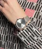 A close-up shot of a woman's wrist wearing a silver watch, with a patterned shirt visible. Voir les images du produit