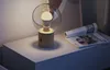 A modern table lamp with a glass shade is placed on a nightstand next to a magazine. Náhled obrázku produktu