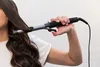 A person is using a curling iron to style their hair. Náhled obrázku produktu