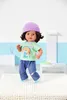 A doll standing on a rug in front of a blue and white background. Produktbild-Vorschau