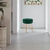 A dark green velvet stool with gold metal legs is placed in a hallway with a painting on the wall. Produktbild-Vorschau